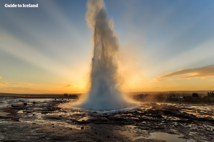 Gejsern Strokkur får utbrott framför solen.
